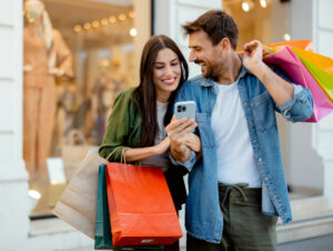 Gl&uuml;ckliches Paar mit Einkaufst&uuml;ten und Smartphone